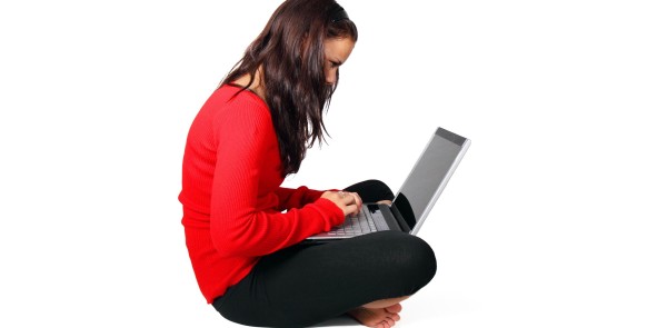 Frau sitzt im Schneidersitz mit einen Laptop auf dem Schoß